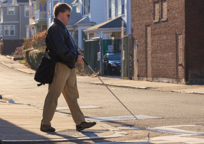 Man with congenital blindness crossing the street using his cane