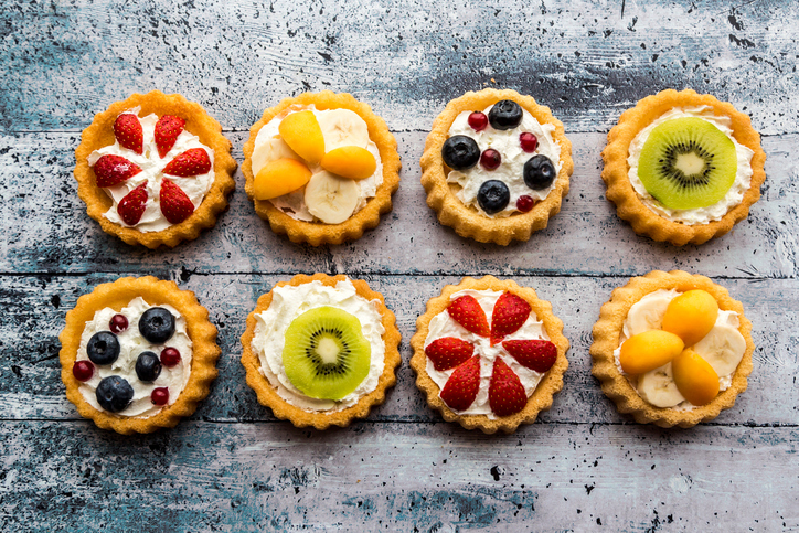 Eight mini pies with whipped cream garnished with different fruits