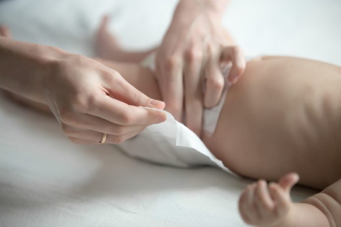 Female hands fixing a diaper on a newborn lying