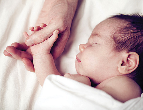 Photo of sleeping newborn baby holding adult thumb to represent newborn genome sequencing to test for treatable genetic disorders.