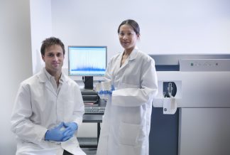 Portati of scientists in front of a mass spectrometer used for molecualr analysis. Proteins are ionised by vaporisation then studied by the relative weight of the different ions