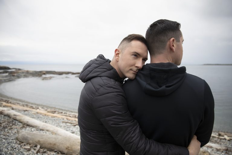 Affectionate, tender male gay couple hugging on beach