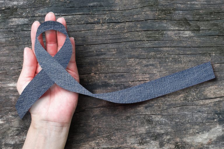 Blue jeans denim ribbon (isolated with clipping path) on helping hand support and aged wood for genetic disorder awareness and children's rare disease illness