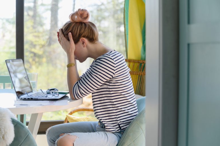 Woman sitting in front of laptop with head in hands to illustrate depression