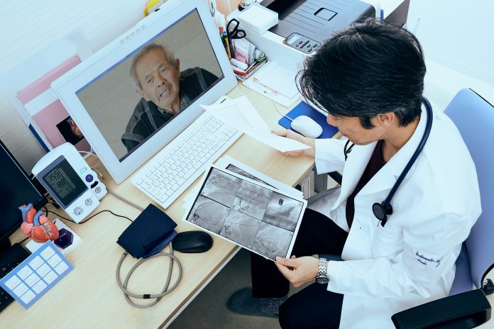 Cardiovascular doctor looking at coronary X-ray output and talking to a patient during telemedicine appointment.