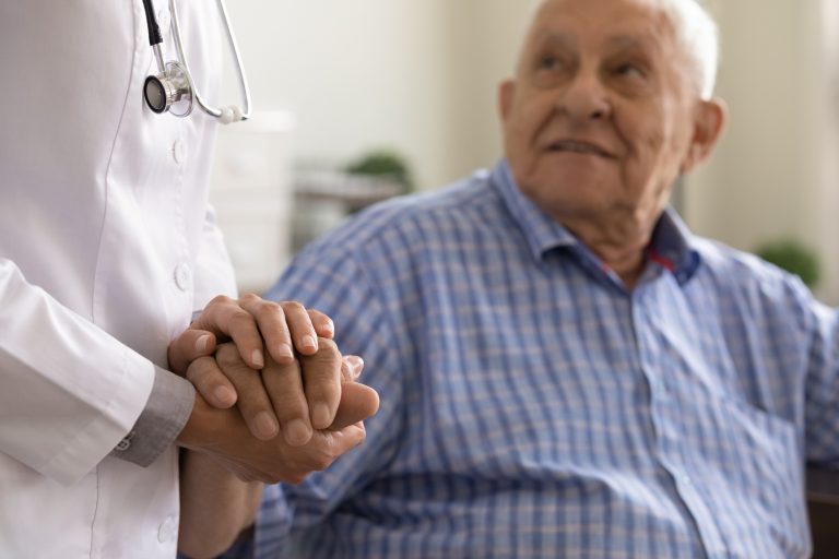 Older white man, with white hair holding the hand of an unseen female healthcare worker with a stethoscope around her neck - image to represent impact of male hormone on aging health
