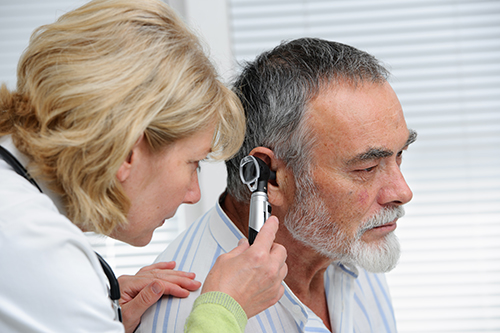 Blond female physician examining an older man's ears to assess hearing loss