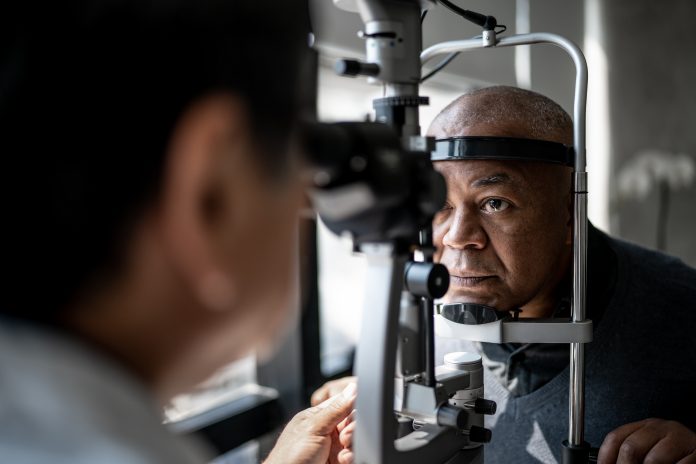 Ophthalmologist examining an older Black, male patient's eyes to carry out retinal imaging to look for inherited retinal diseases using Eye2Gene.