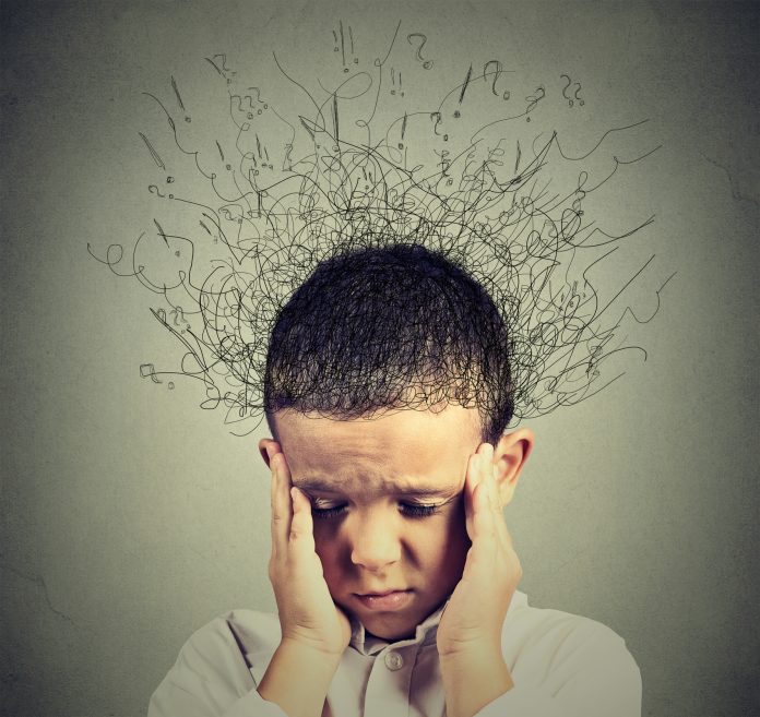 boy with worried stressed face expression looking down with his hands pressed to either side of his face and with chaotic brain waves streaming out of his head to represent ADHD