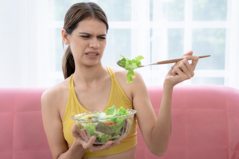 Unhappy young Caucasian woman does not want to eat vegetables and does not like the bitter taste of vegetables.