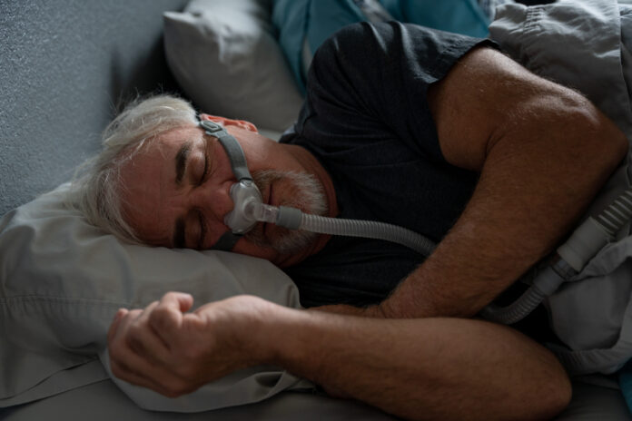 Mature Man With Sleep Apnea Wearing A CPAP Mask In Bed Sleeping