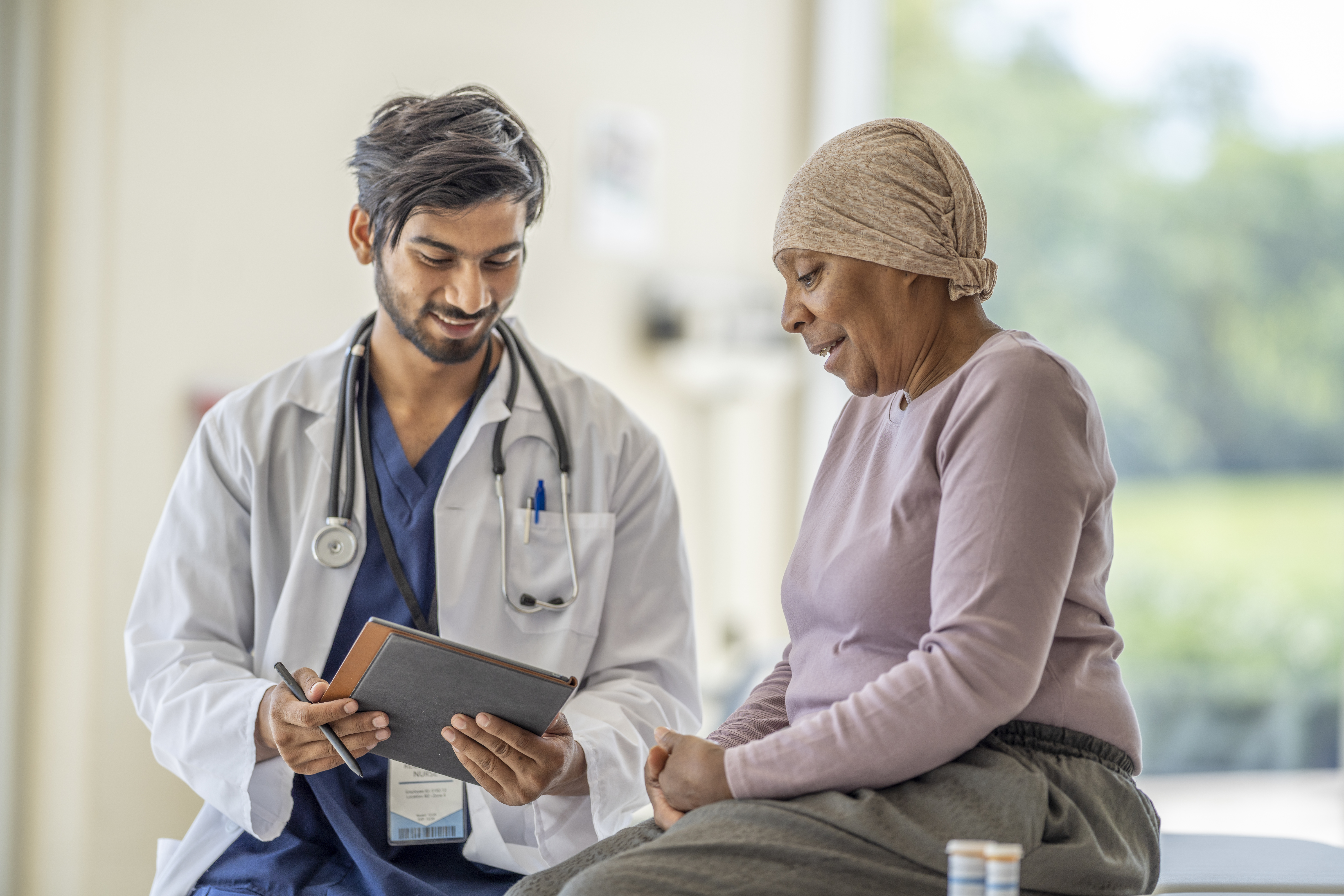 Middle Eastern appearance male oncologist talking to an older Black Female Patient about Claudin18.2 related CAR T cell and cancer vaccine therapies.