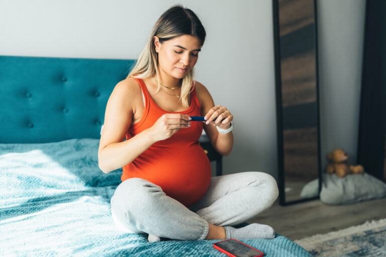 Pregnant young woman sitting on a bed preparing insulin dosage in insulin pen before injecting to represent gestational diabetes
