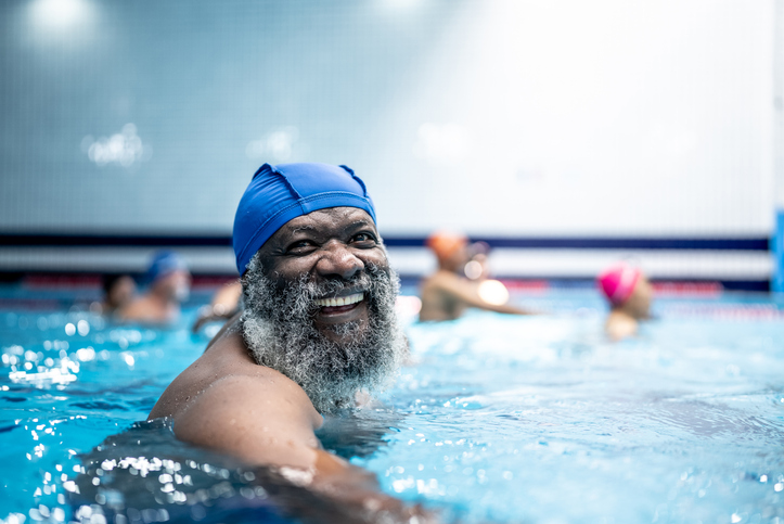 Portrait of an older black man in a swimming pool wearing a swimming hat. Exercise is one of several lifestyle factors that can help increase lifespan.