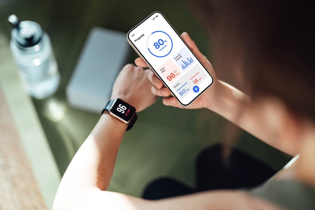 Overhead of young woman using fitness app on smartphone and smartwatch to monitor training progress after exercising at home