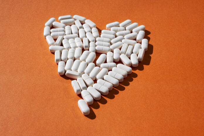 Minerals and trace elements for heart health. The shape of the heart is laid out of white oval tablets on an orange background. Nutraceuticals and sublimates for health.