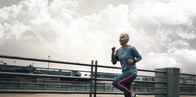 Mature, short haired, woman running in the city in sports clothing looking away to symbolize exercising to help recovery after breast cancer